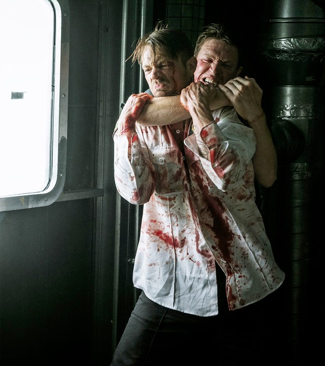 Um aus dem Gefängnis zu entkommen, attackiert Pete Koslow (Joel Kinnaman, l.) den korrupten Wärter Slewitt (Sam Spruell, r.). "The Informer - Wettlauf gegen die Zeit": Pete Koslow (Joel Kinnaman) und Slewitt (Sam Spruell) kämpfen miteinander. Petes Hemd ist voller Blut und Slewitt würgt ihn von hinten.