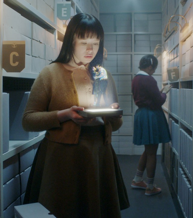 "The Ordinaries": Paula (Fine Sendel) steht im Gang eines Archivs und schaut auf ein Hologramm, welches sie in ihren Händen hält.  