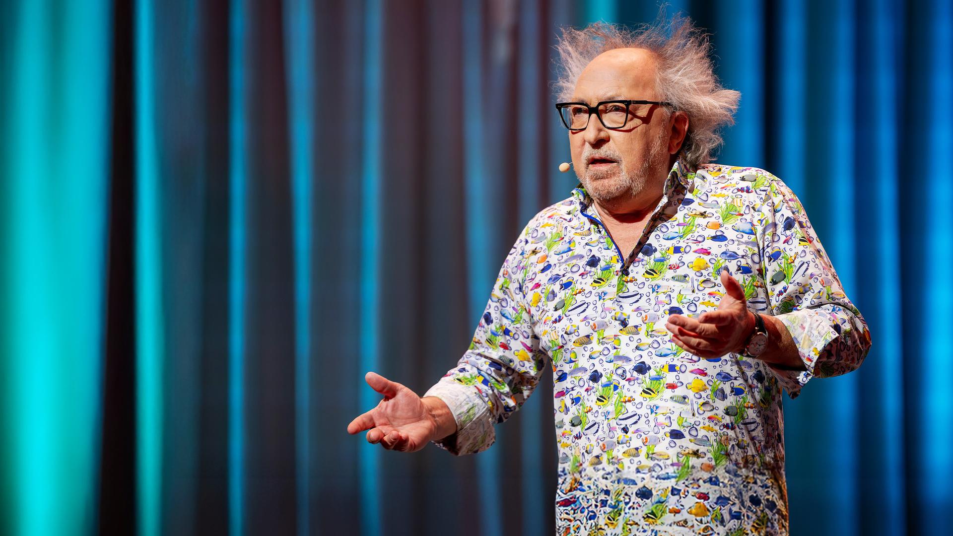 Urban Priol steht auf der Bühne. Er trägt ein buntes Hemd mit kleinen Fischen darauf.