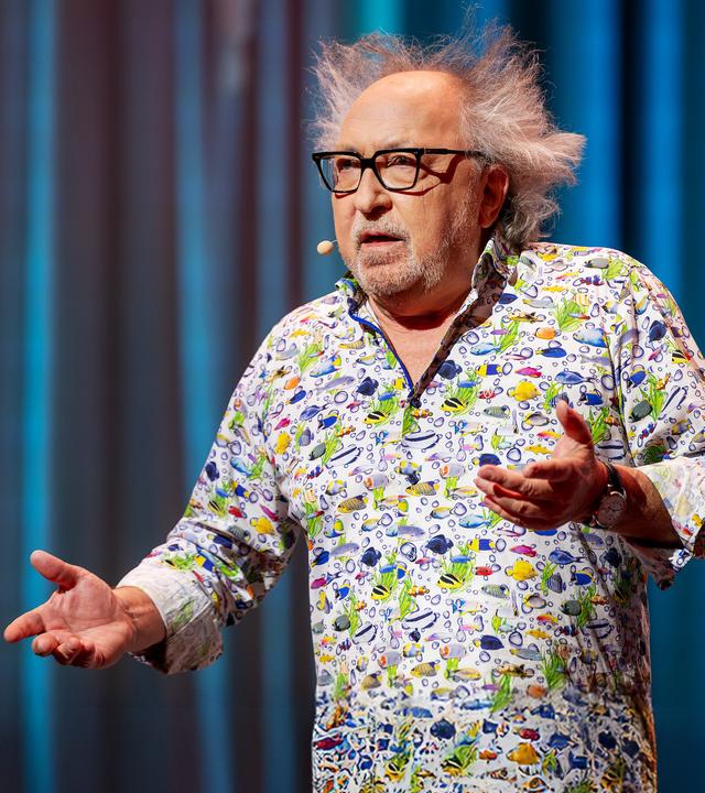 Urban Priol steht auf der Bühne. Er trägt ein buntes Hemd mit kleinen Fischen darauf.
