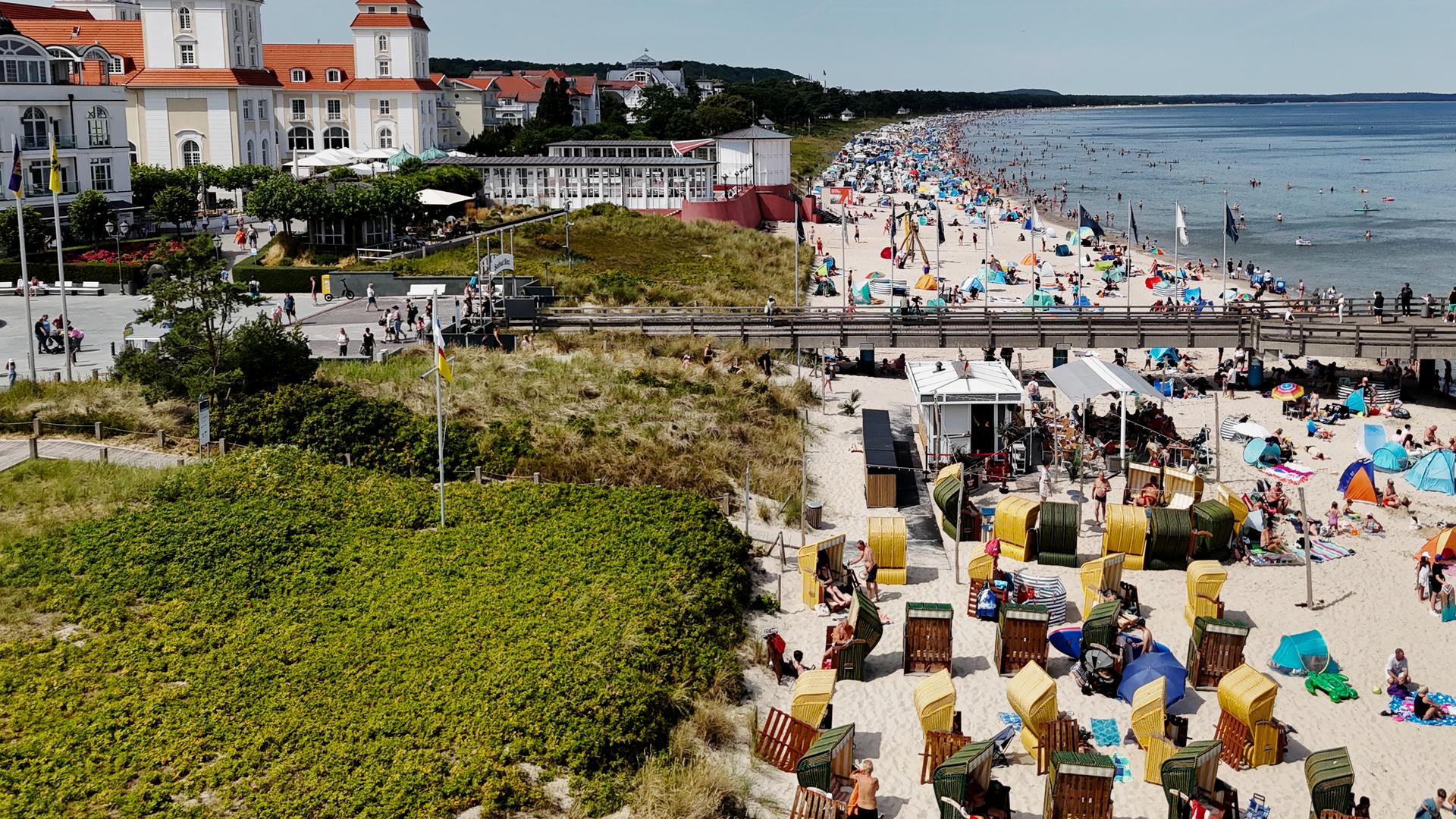 Urlauber am Strand mit Sonnenschirmen und in Strandkörben auf der Insel Rügen mit Hotel im Hintergrund