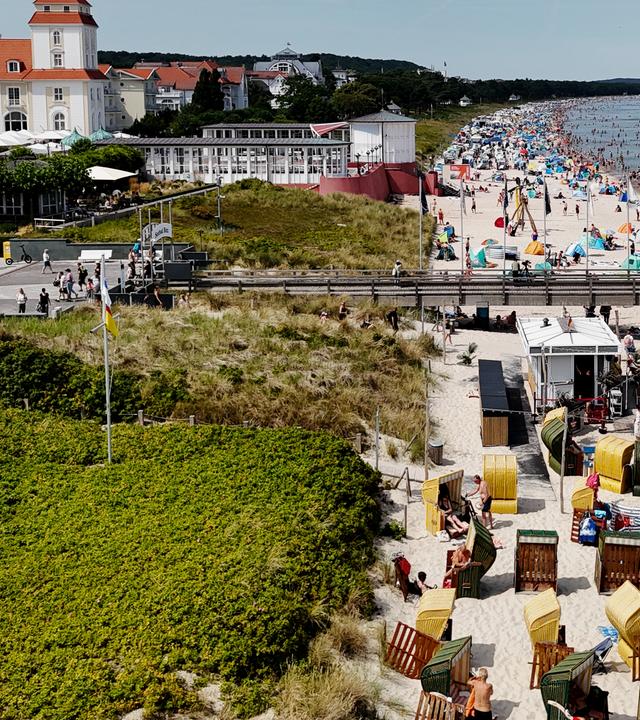 Urlauber am Strand mit Sonnenschirmen und in Strandkörben auf der Insel Rügen mit Hotel im Hintergrund