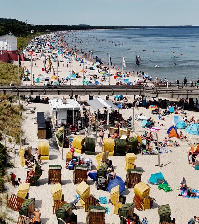 Urlauber am Strand mit Sonnenschirmen und in Strandkörben auf der Insel Rügen mit Hotel im Hintergrund