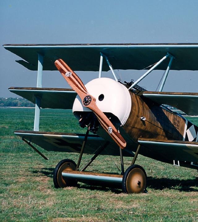 Ein Dreidecker des Types "Fokker Dr.I" steht auf einer Graswiese.
