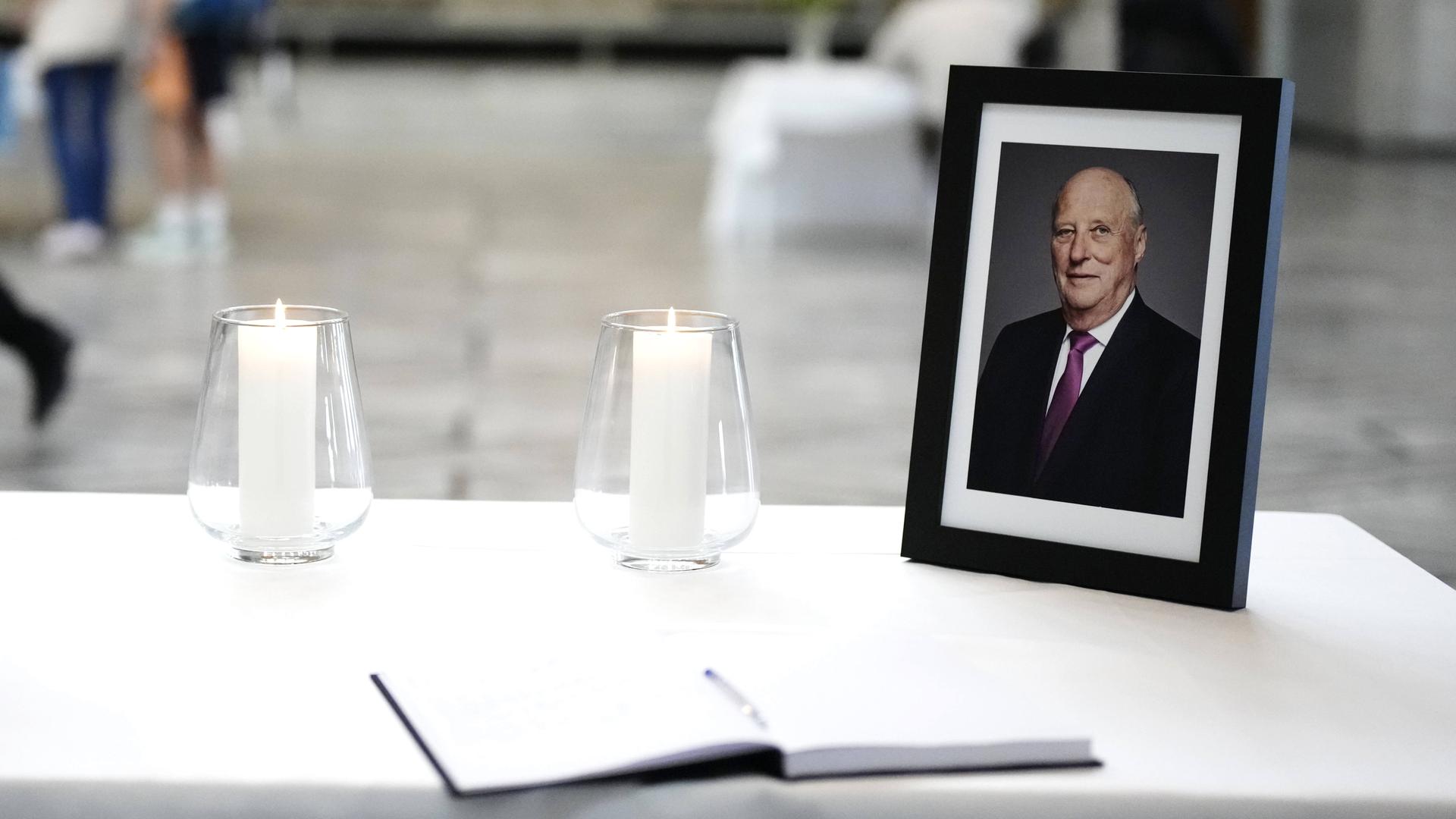 Ein Foto von König Harald steht in einem schwarzen Bilderrahmen neben einer Kerze auf einem Tisch