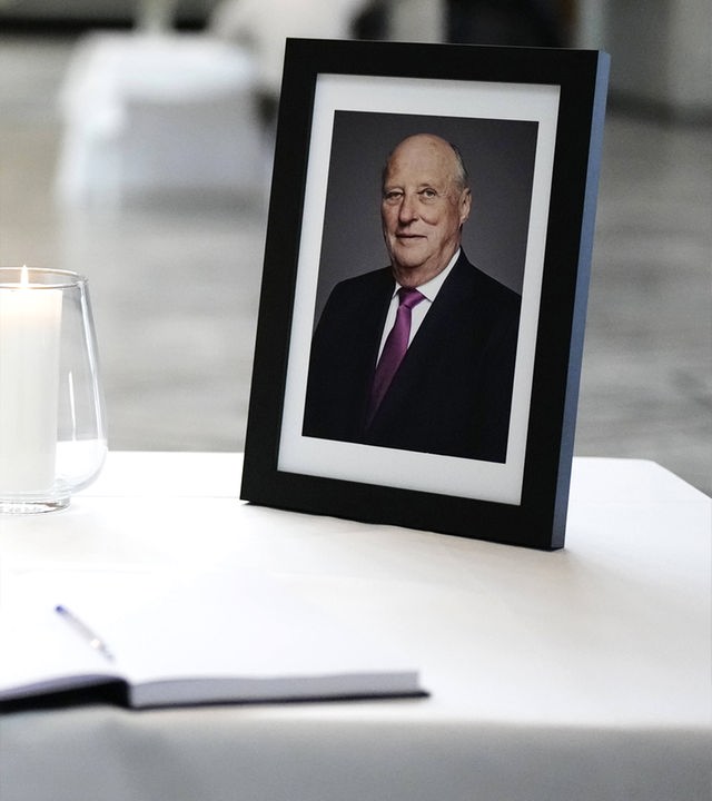 Ein Foto von König Harald steht in einem schwarzen Bilderrahmen neben einer Kerze auf einem Tisch