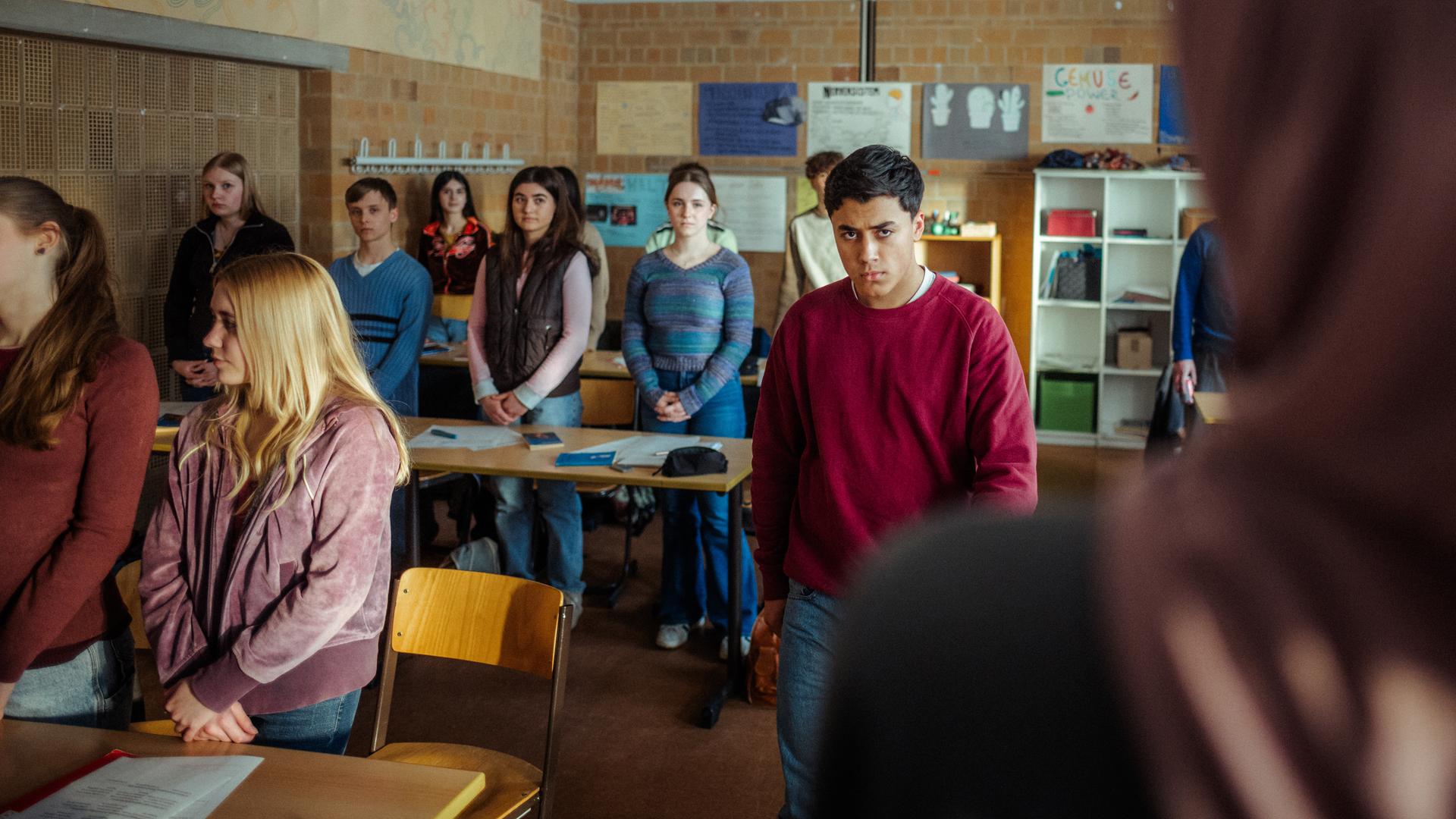 "Uncivilized - Nine Eleven": Ahmad (Rasmi Mohammed Nasrallah) verlässt wütend den Klassenraum, während seine Mitschülerinnen und Mitschüler mit gefalteten Händen an Ihren Plätzen stehen.