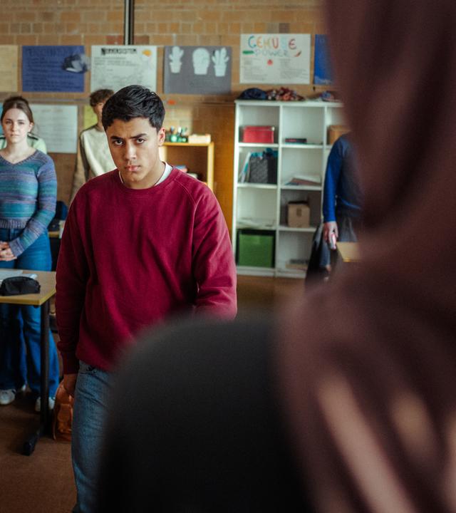 "Uncivilized - Nine Eleven": Ahmad (Rasmi Mohammed Nasrallah) verlässt wütend den Klassenraum, während seine Mitschülerinnen und Mitschüler mit gefalteten Händen an Ihren Plätzen stehen.