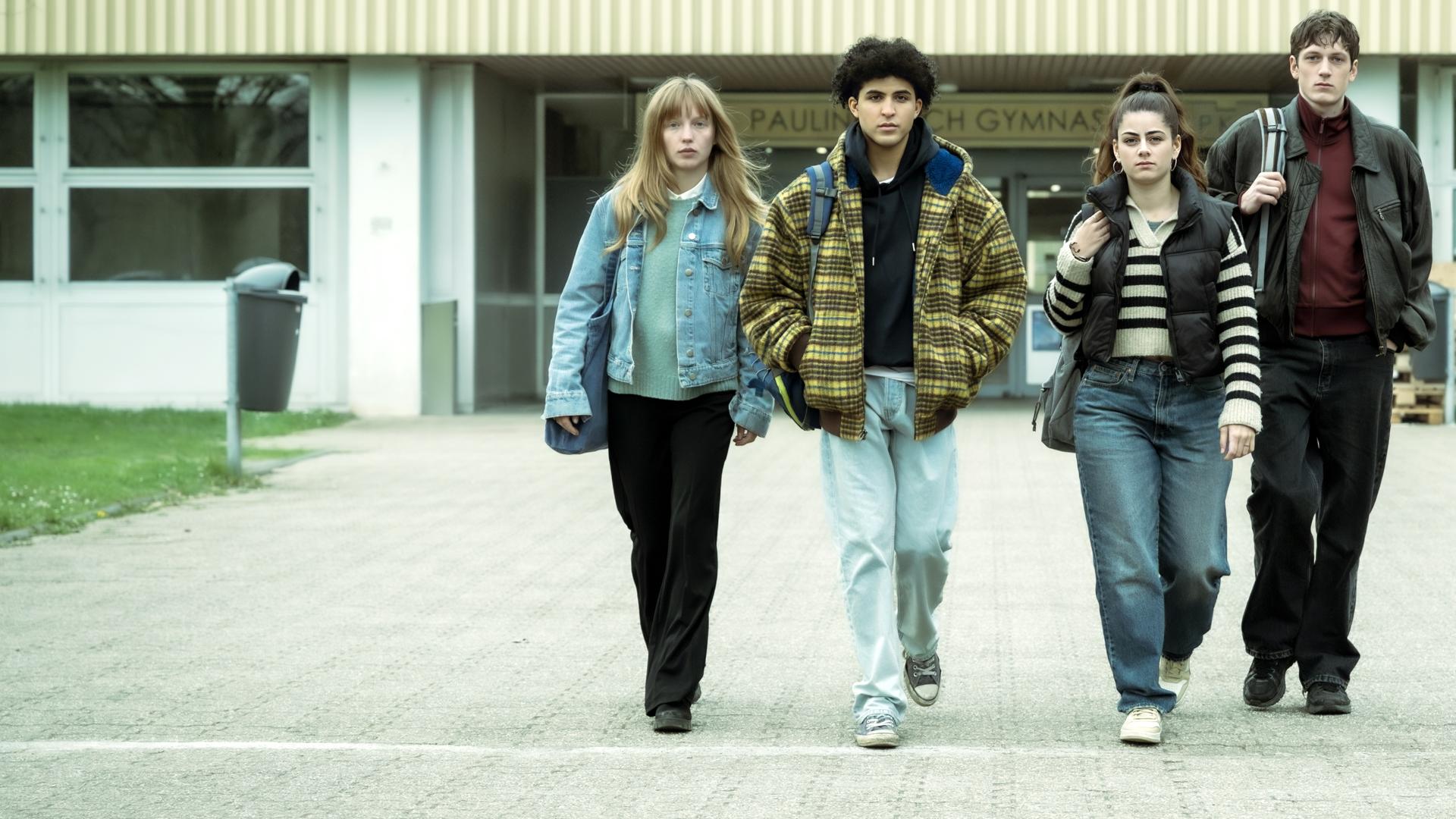 Julia (Mina-Giselle Rüffer), Waldi (Lukas von Horbatschewsky), Mina (Derya Akyol) und Tom (Kosmas Schmidt) entfernen sich vom Schuleingang und laufen zusammen über das Schulgelände in Richtung Kamera.