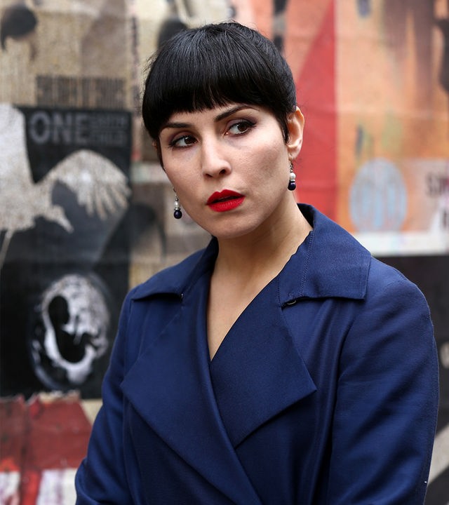 Monday (Noomi Rapace) steht vor einer plakatierten Mauer und sieht zur Seite.