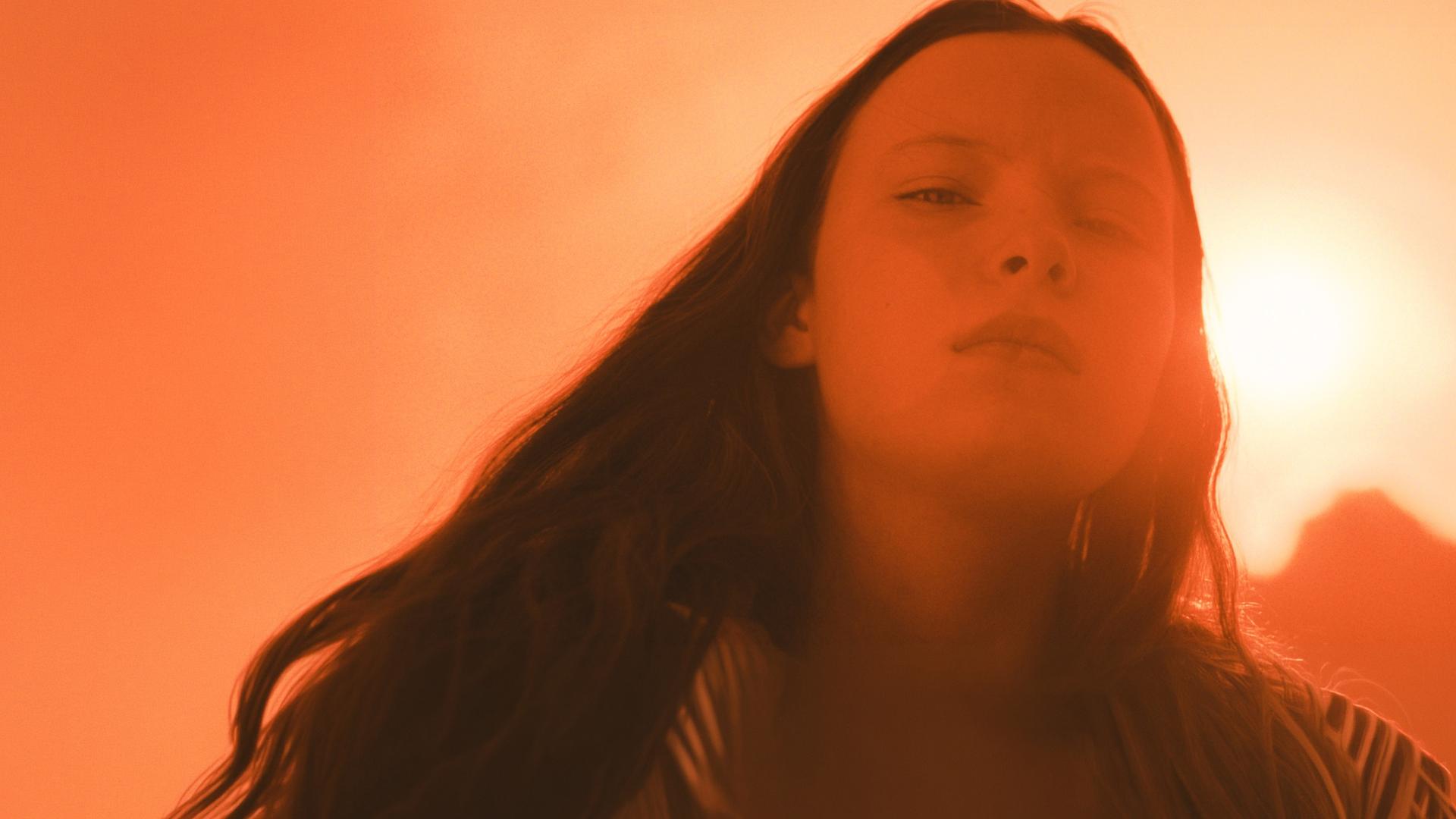 Marielle (Laeni Geiseler) schaut von oben herab in dei Kamera. Hinter ihr scheint die Sonne.