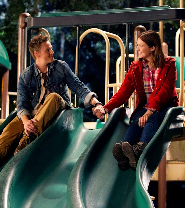 ommy (Riley Smith l.) und Natalie (Mandy Moore r.) sitzen auf der Rutsche eines Kinderspielplatzes. Sie halten ihre Hände und schauen sich dabei in die Augen. Es ist Abend.