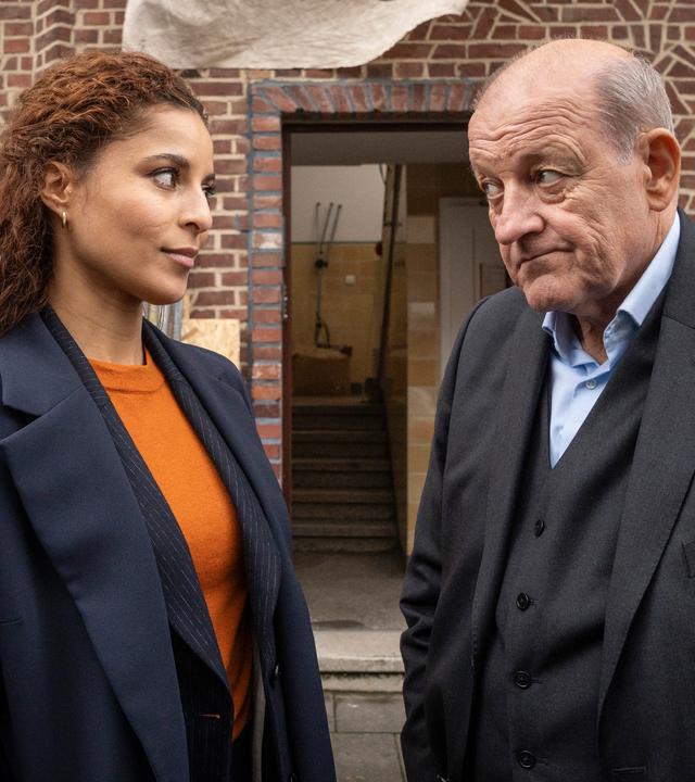 Wilsberg (Leonard Lansink) und Tessa Tilker (Patricia Meeden) stehen vor einem Mehrfamilienhaus, das sich im Umbau befindet.