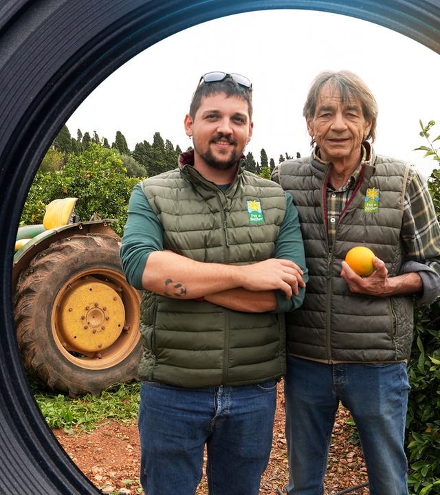 Franz Kraus und Stefan Livida stehen vor einem Traktor. Im Hintergrund stehen Orangenbäume.