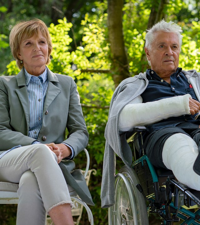 Dorothee (Ulrike Kriener) sitzt auf einer Bank im Grünen neben Volker (Henry Hübchen), der im Rollstuhl sitzt.