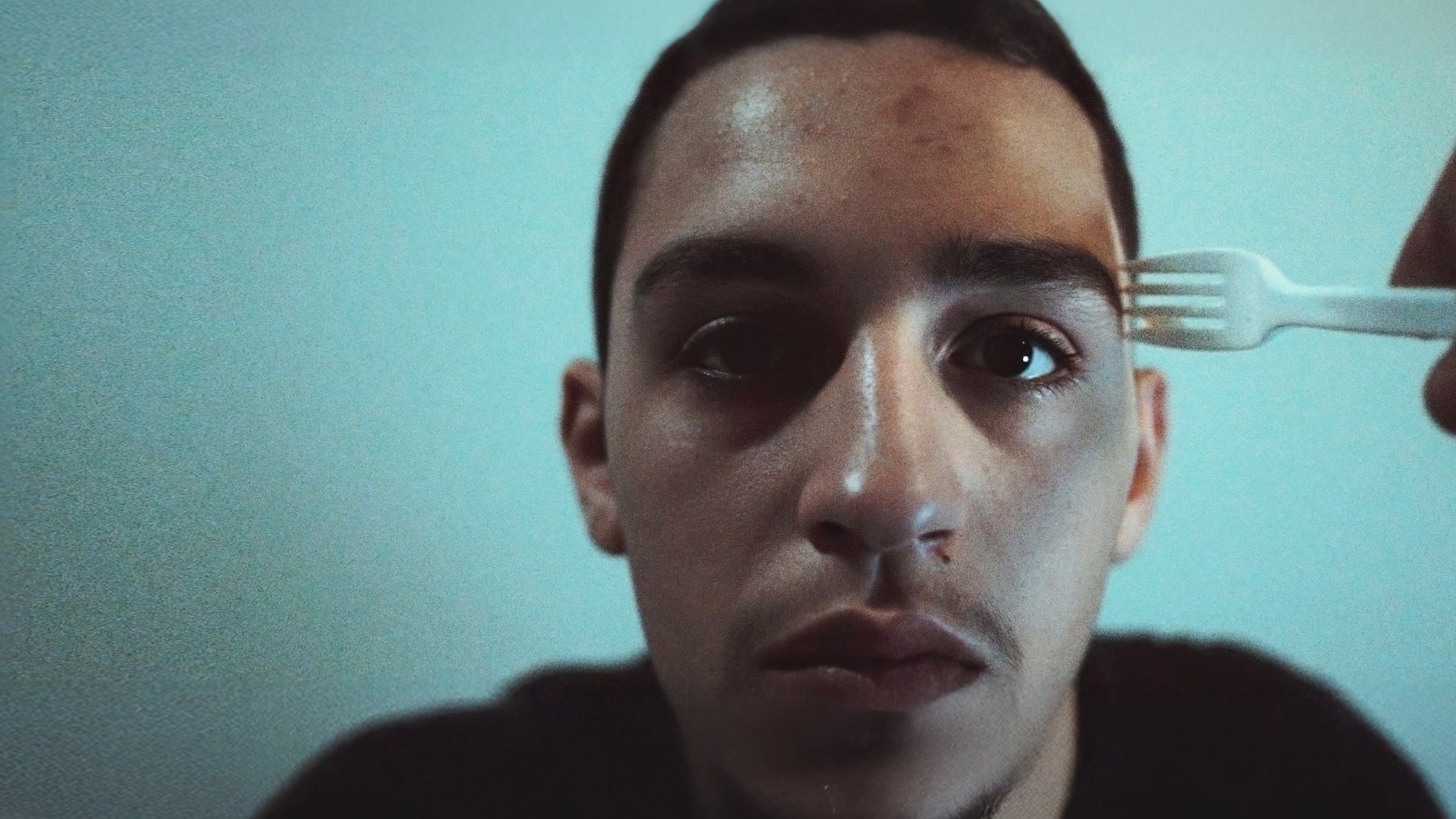 Nasser (Abdulrahman Diab) wartet auf die Entscheidung über seinen Asylantrag. "Xoftex": Nasser, ein junger Mann, schaut nach vorne. Eine Gabel wird an seine Schläfe gehalten.