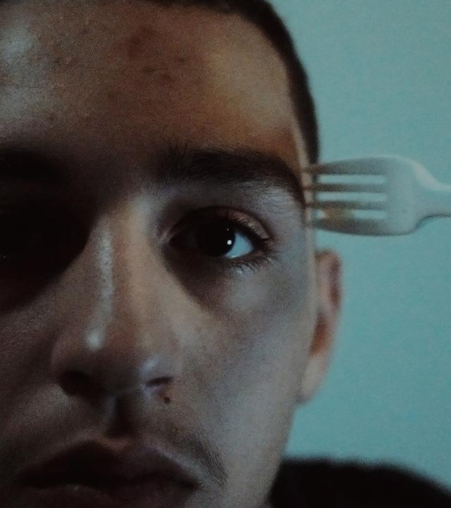 Nasser (Abdulrahman Diab) wartet auf die Entscheidung über seinen Asylantrag. "Xoftex": Nasser, ein junger Mann, schaut nach vorne. Eine Gabel wird an seine Schläfe gehalten.