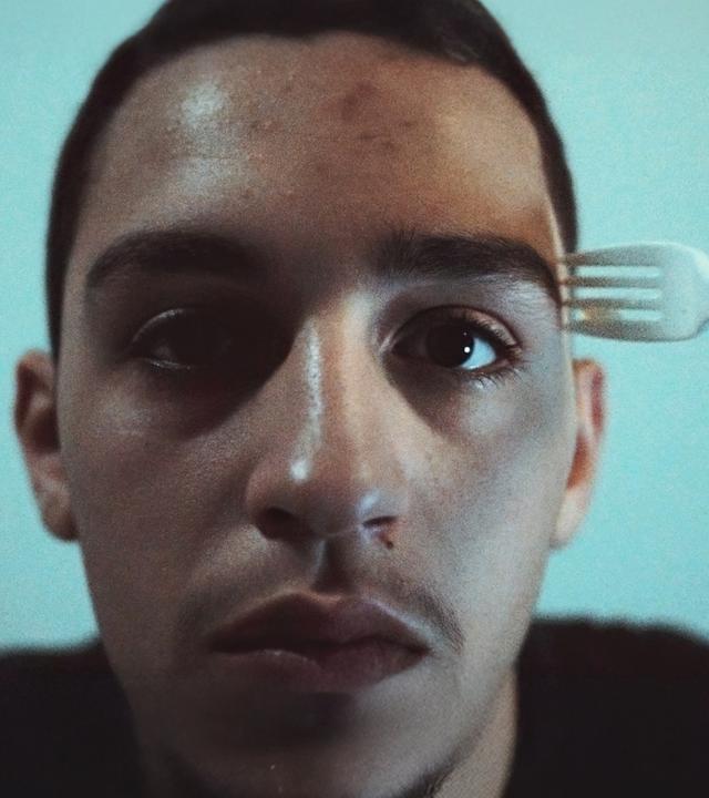 Nasser (Abdulrahman Diab) wartet auf die Entscheidung über seinen Asylantrag. "Xoftex": Nasser, ein junger Mann, schaut nach vorne. Eine Gabel wird an seine Schläfe gehalten.