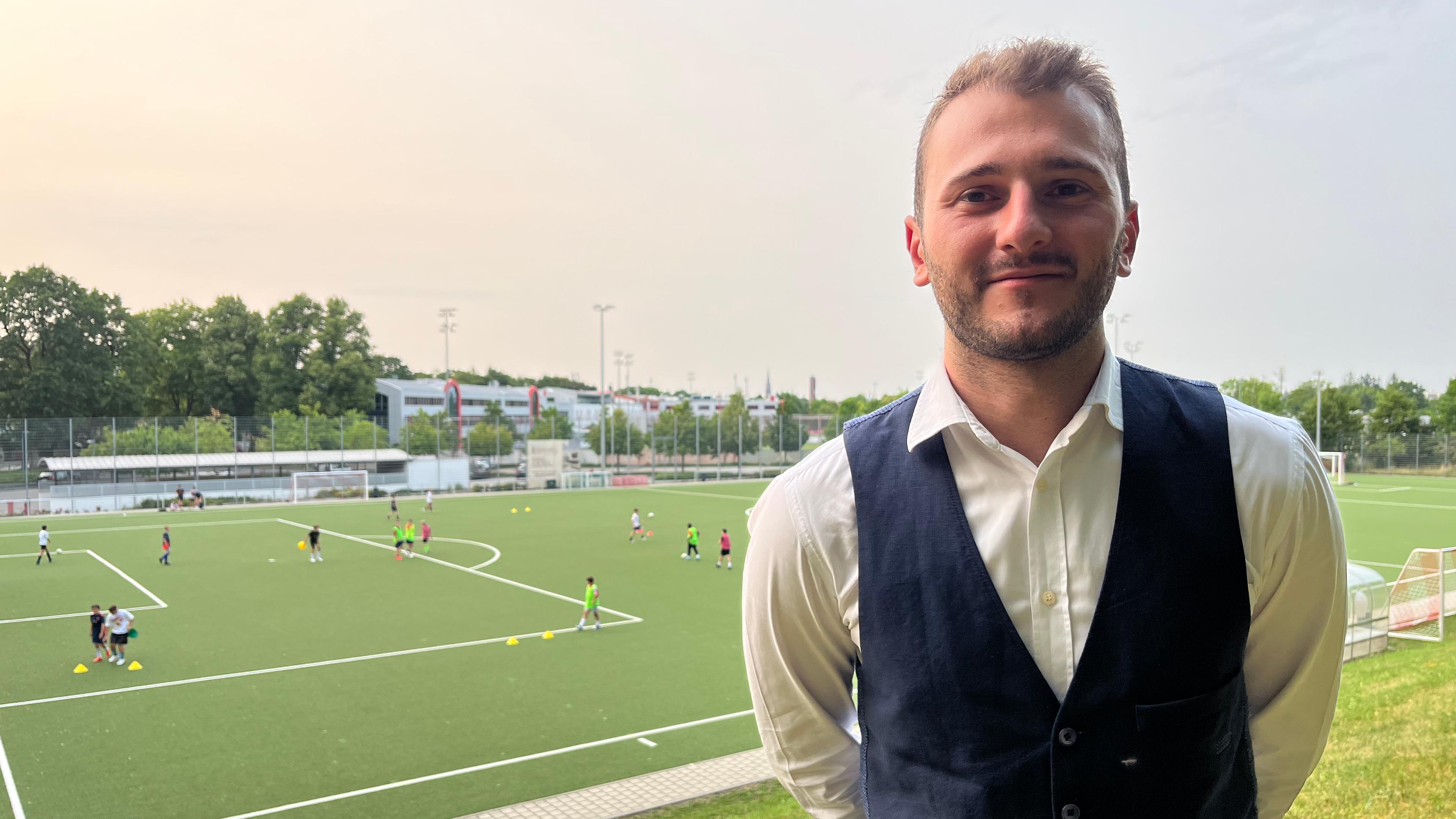 Herrlin Markja, 1. Vorsitzender des FC Sportfreunde München, steht vor dem Fußballplatz seines Klubs