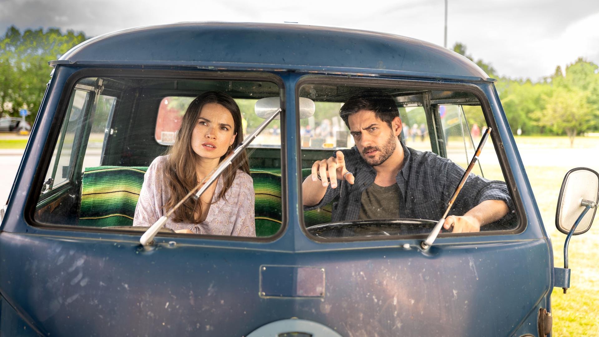 "Inga Lindström: Herz über Kopf": Nora (Zoe Moore) und Samu (Félix Herzog) sitzen auf den Vordersitzen eines alten VW-Busses und beobachten etwas in der Ferne.
