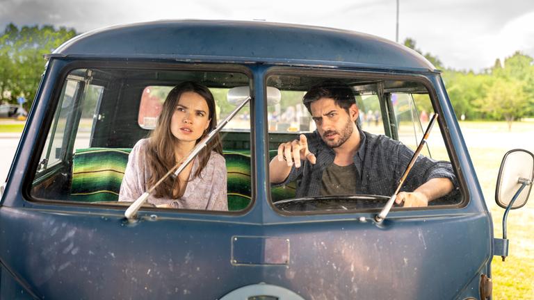 "Inga Lindström: Herz über Kopf": Nora (Zoe Moore) und Samu (Félix Herzog) sitzen auf den Vordersitzen eines alten VW-Busses und beobachten etwas in der Ferne.