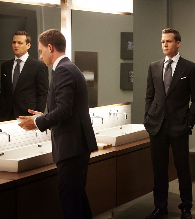 "Suits - Herzenssache": In einem Toilettenraum: Mike (Patrick J. Adams) steht an einem Waschtisch vor einem großen Spiegel, während Harvey (Gabriel Macht) mit ernster Miene im Raum steht und ihn beobachtet.