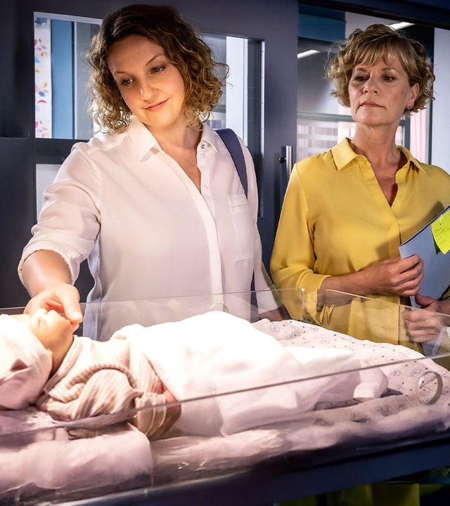Svenja Richnow (Victoria Fleer) und Karin Berger (Anne Kasprik) stehen nebeneinander neben dem Bettchen eines Neugeborenen.
