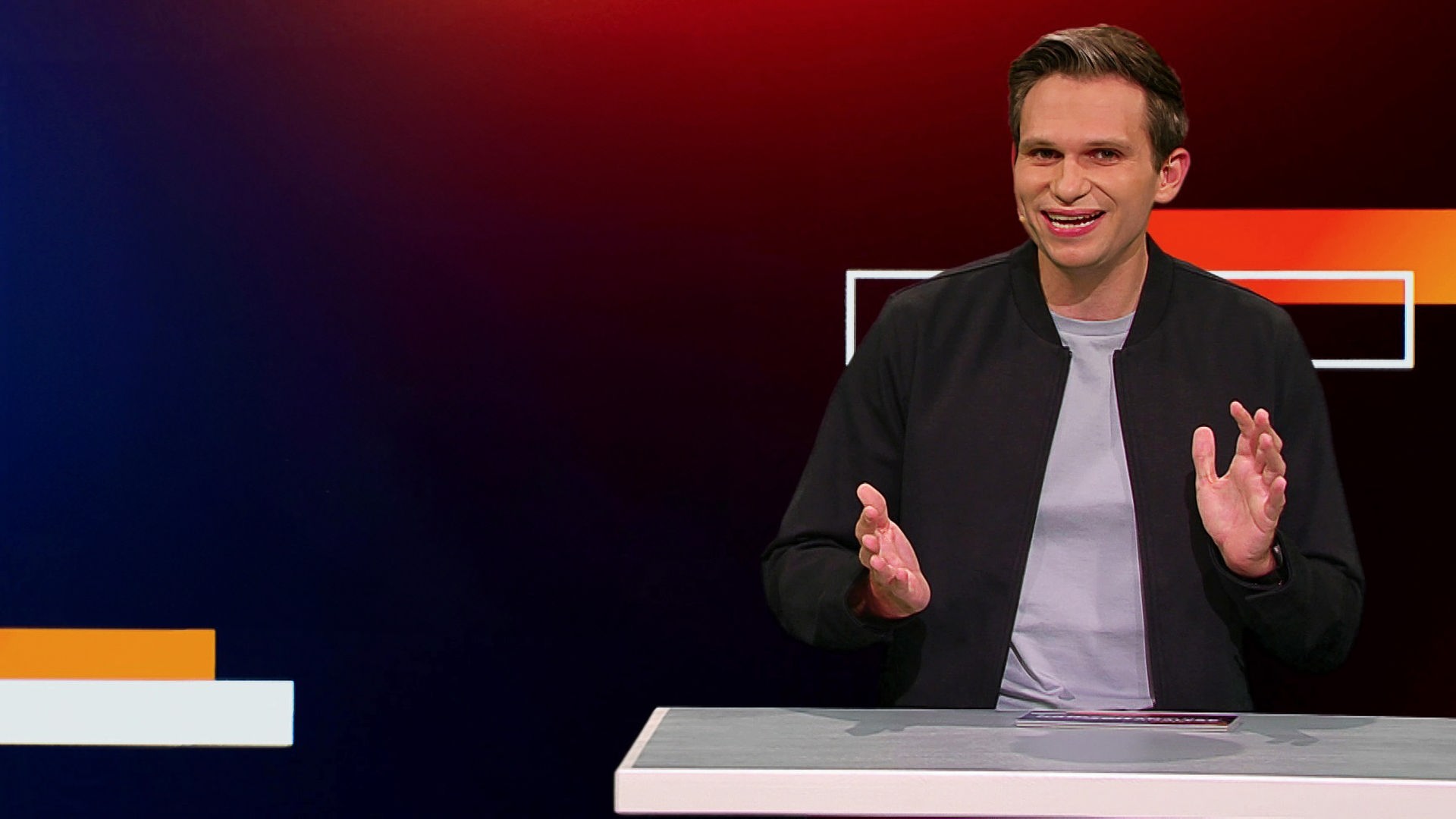 Fabian Köster sitzt in einem Studio an einem Schreibtisch. Links von ihm ist eine satirische Fotomontage von Friedrich Merz als Schiedsrichter zu sehen, der auf einen verletzten Fußballspieler zeigt, der auf dem Rasen liegt. Am unteren Bildrand steht "Faul!".