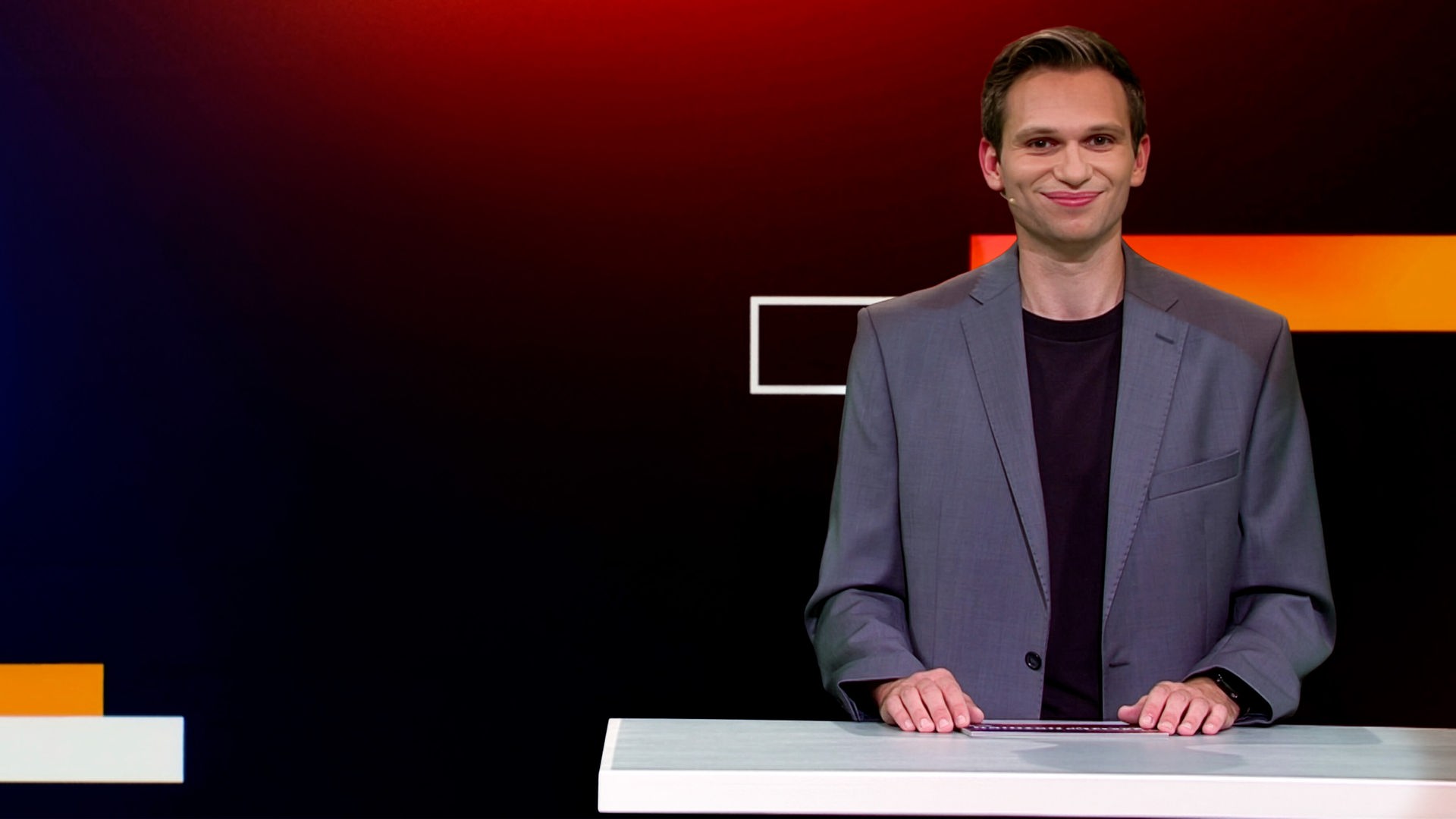 Fabian Köster sitzt in einem Studio an einem Schreibtisch. Links von ihm ist eine satirische Fotomontage von Alice Weidel und Tino Chrupalla zu sehen, die auf Wladimir Putins Schoß sitzen, während Putin aus einem Buch vorliest. Am unteren Bildrand steht "PUTIN ANTE PORTAS".