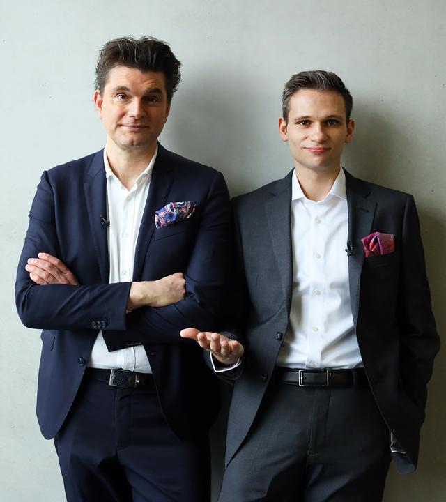 Lutz van der Horst und Fabian Köster stehen vor einer weißen Wand und lächeln in die Kamera.