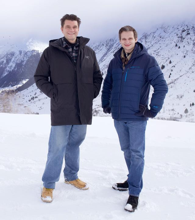 Lutz van der Horst und Fabian Köster stehen im Schnee des Skigebietes Galtür, im Hintergrund sind Teile der Silvretta-Gebirgsgruppe zu sehen.