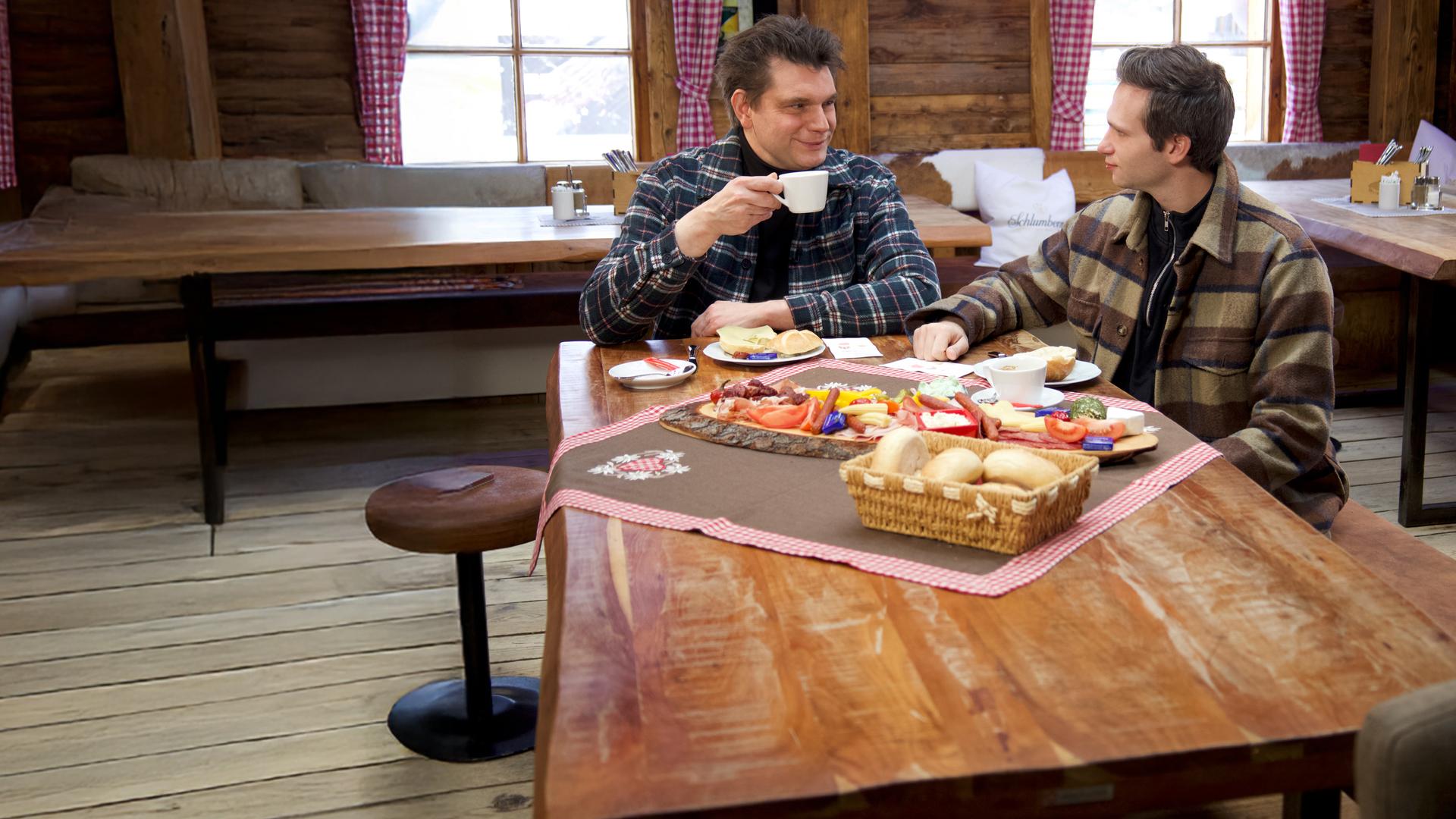 Lutz van der Horst (l.) und Fabian Köster (r.) sitzen an einem Tisch, der mit einer Brotzeit gedeckt ist.