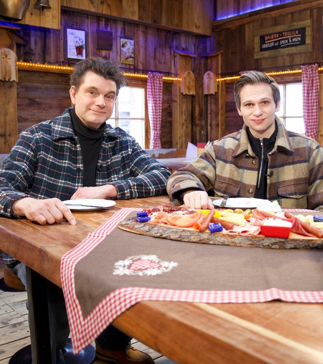 Lutz van der Horst (l.) und Fabian Köster (r.) sitzen an einem Tisch, der mit einer Brotzeit gedeckt ist.