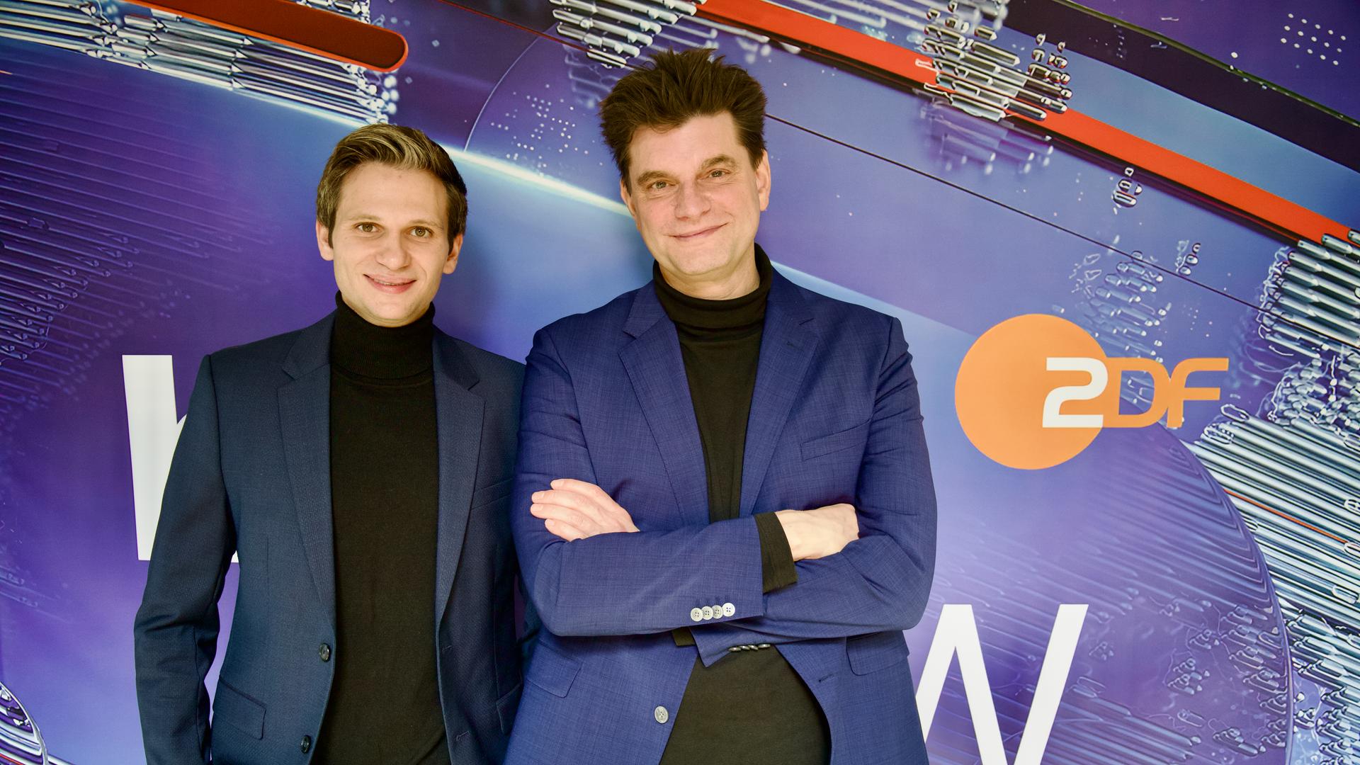 Fabian Köster (l.) und Lutz van der Horst (r.) posieren vor dem "heute-show"-Logo. Sie tragen beide einen Anzug.