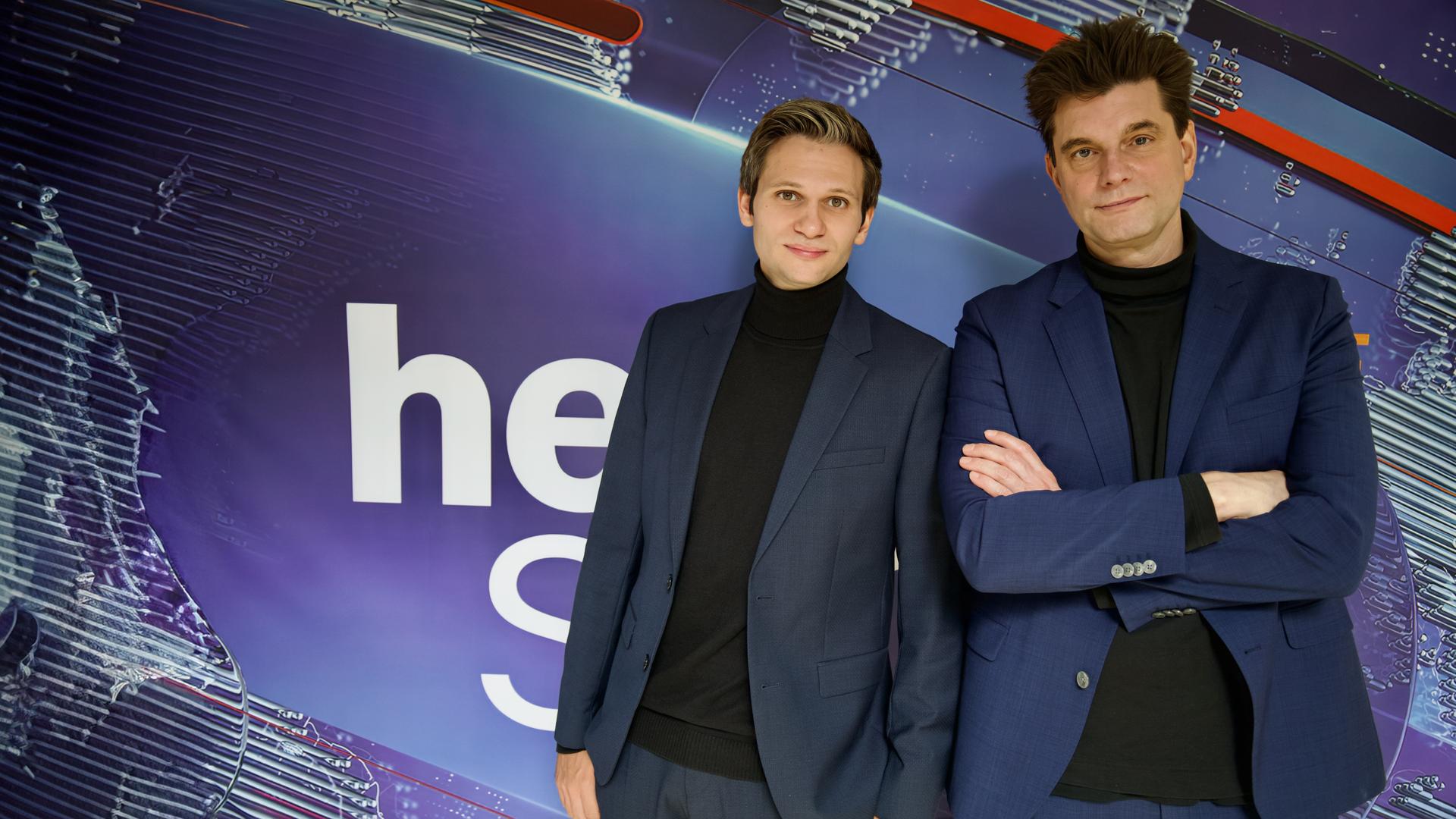 Fabian Köster (l.) und Lutz van der Horst (r.) posieren vor dem "heute-show"-Logo. Sie tragen beide einen Anzug.