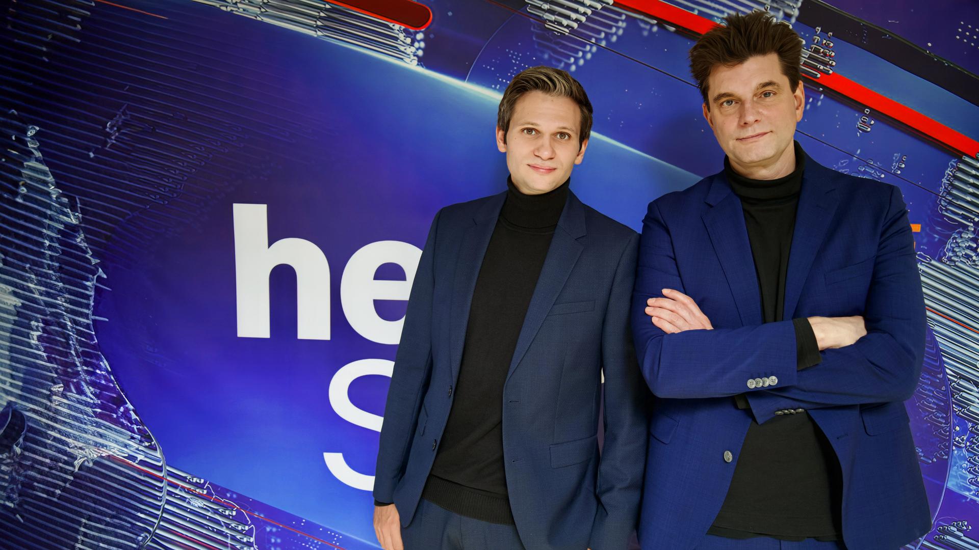 Fabian Köster (l.) und Lutz van der Horst (r.) posieren vor dem "heute-show"-Logo. Sie tragen beide einen Anzug.