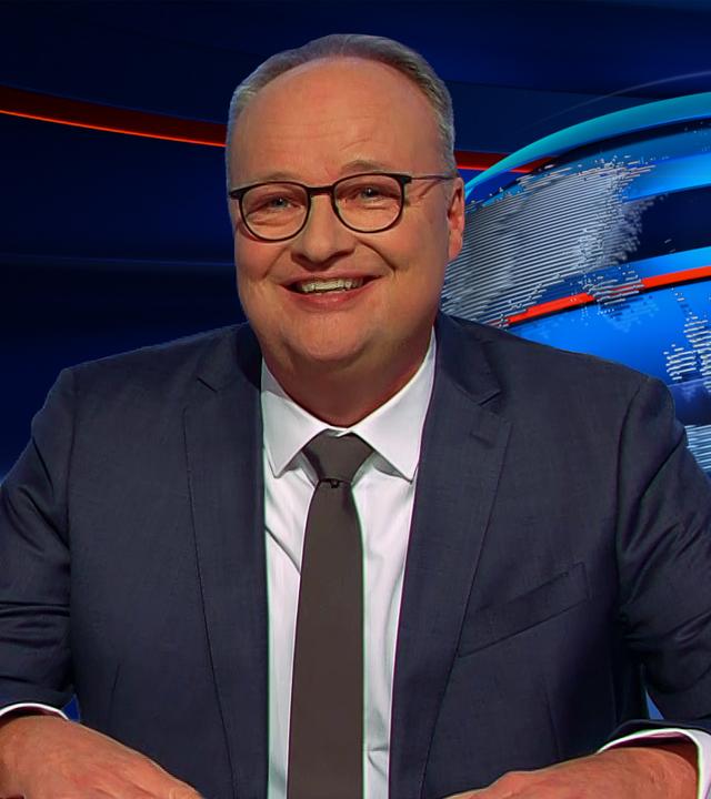 Oliver Welke sitzt rechts im Bild. Links im Bild ist eine satirische Fotomontage zu sehen: Friedrich Merz und Lars Klingbeil sitzen auf einem Sofa in einem verwahrlosten Wohnzimmer. Zwischen ihnen hängt ein gerahmtes Porträtfoto von Olaf Scholz. Unter dem Bild steht: "WIE BEI AMPELS UNTERM SOFA".