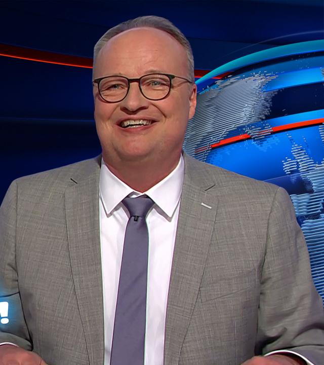 Oliver Welke sitzt am Schreibtisch. Links im Hintergrund ist eine Fotocollage mit mehreren euphorischen Menschen an einer Tankstelle abgebildet. Darunter steht: 17 Cent wir sind gerettet!