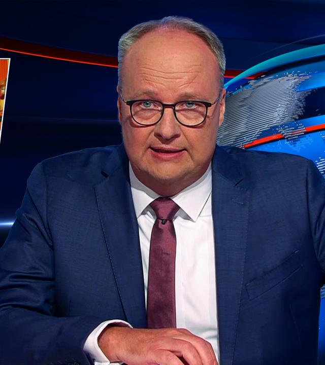 Oliver Welke sitzt am Schreibtisch. Links von ihm ist ein Bild zu sehen, auf dem Donald und Melania Trump in schmuddeliger Kleidung neben König Charles und Königin Camilla stehen. Am unteren Rand des Bildes steht der Text: "Die Flodders in England".