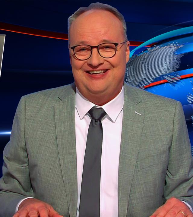 Oliver Welke sitzt am Schreibtisch. Links von ihm ist eine Fotomontage eines Magazincovers im Retro-Stil zu sehen, auf dem steht "Bild der Frau von vorgestern". Auf dem Cover ist Friedrich Merz mit Pfeife abgebildet, während im Hintergrund eine Frau in einer Küche arbeitet.