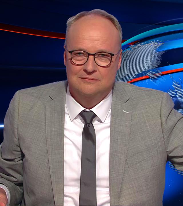 Oliver Welke sitzt an einem Schreibtisch. Links von ihm ist eine Fotocollage zu sehen, die eine MAGGI Fix Packung parodiert. Die Vorderseite zeigt Friedrich Merz als Koch und der Text darauf lautet "Nix is fix für Koalitionsverträge".