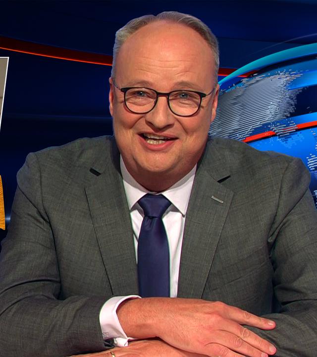 Oliver Welke sitzt am Schreibtisch. Links neben ihm ist ein Bild von Friedrich Merz zu sehen, der mit erhobenen Armen und Pompons in beiden Händen nach oben springt. Darunter steht: "Go, Wirtschaft, Go!"