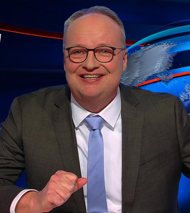 Oliver Welke sitzt am Schreibtisch. Links neben ihm ist eine Fotomontage abgebildet, die an die Serie "The Last of Us" angelehnt ist: Lars Klingbeil und Bärbel Bas befinden sich in einem zerstörten Stadtbild. Darüber steht der Schriftzug "THE LARS OF US".