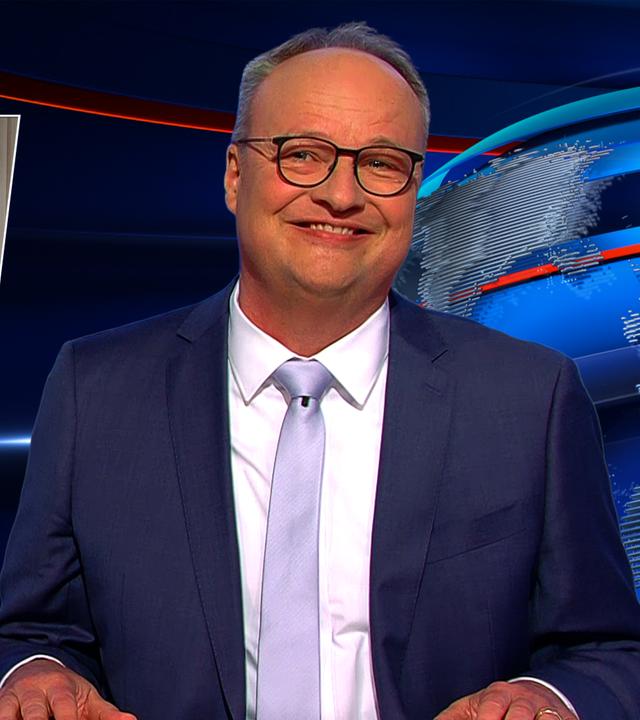 Oliver Welke sitzt am Schreibtisch. Links im Hintergrund ist eine satirische Fotomontage von Friedrich Merz als römischem Herrscher zu sehen. Rechts im Bild steht Hendrik Wüst hinter einem roten Vorhang. Am unteren Bildrand steht "Die Iden des Merz".