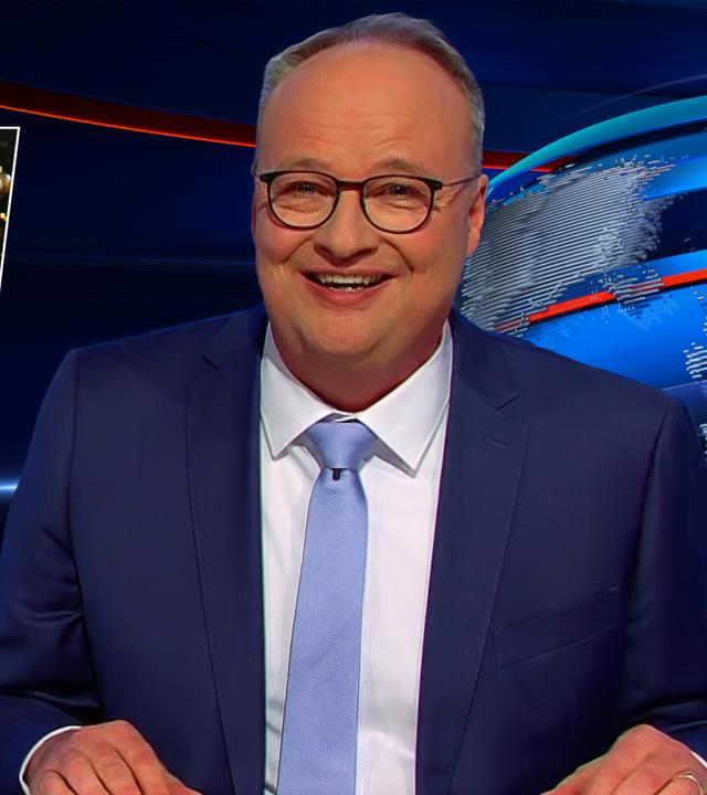 Oliver Welke sitzt am Schreibtisch. Links von ihm ist eine Fotomontage von Friedrich Merz in einem Nikolauskostüm zu sehen, der in erschöpfter Haltung auf einem Stuhl sitzt. Unter dem Bild steht: An Nikolaus fast GroKo-Aus.