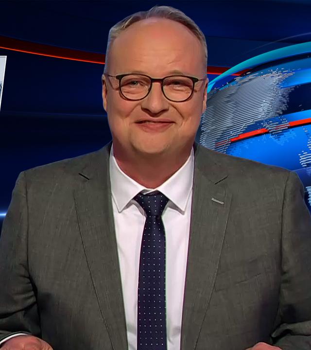 Oliver Welke sitzt am Schreibtisch. Links neben ihm ist eine Fotomontage von Friedrich Merz im Cockpit eines Flugzeugs zu sehen. Darunter steht: "Abgehobene Mittelschicht".