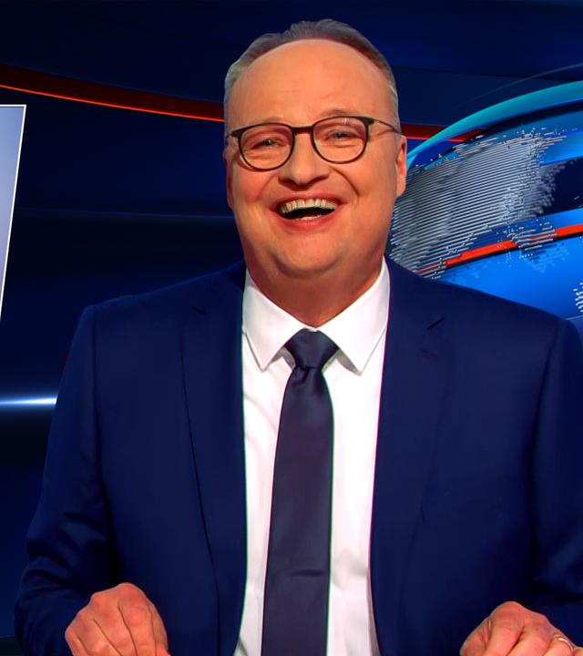 Oliver Welke sitzt am Schreibtisch. Links neben ihm ist eine Fotomontage von Lars Klingbeil und Friedrich Merz in Cheerleader-Outfits zu sehen. Darunter steht "GO AUFSCHWUNG GO".