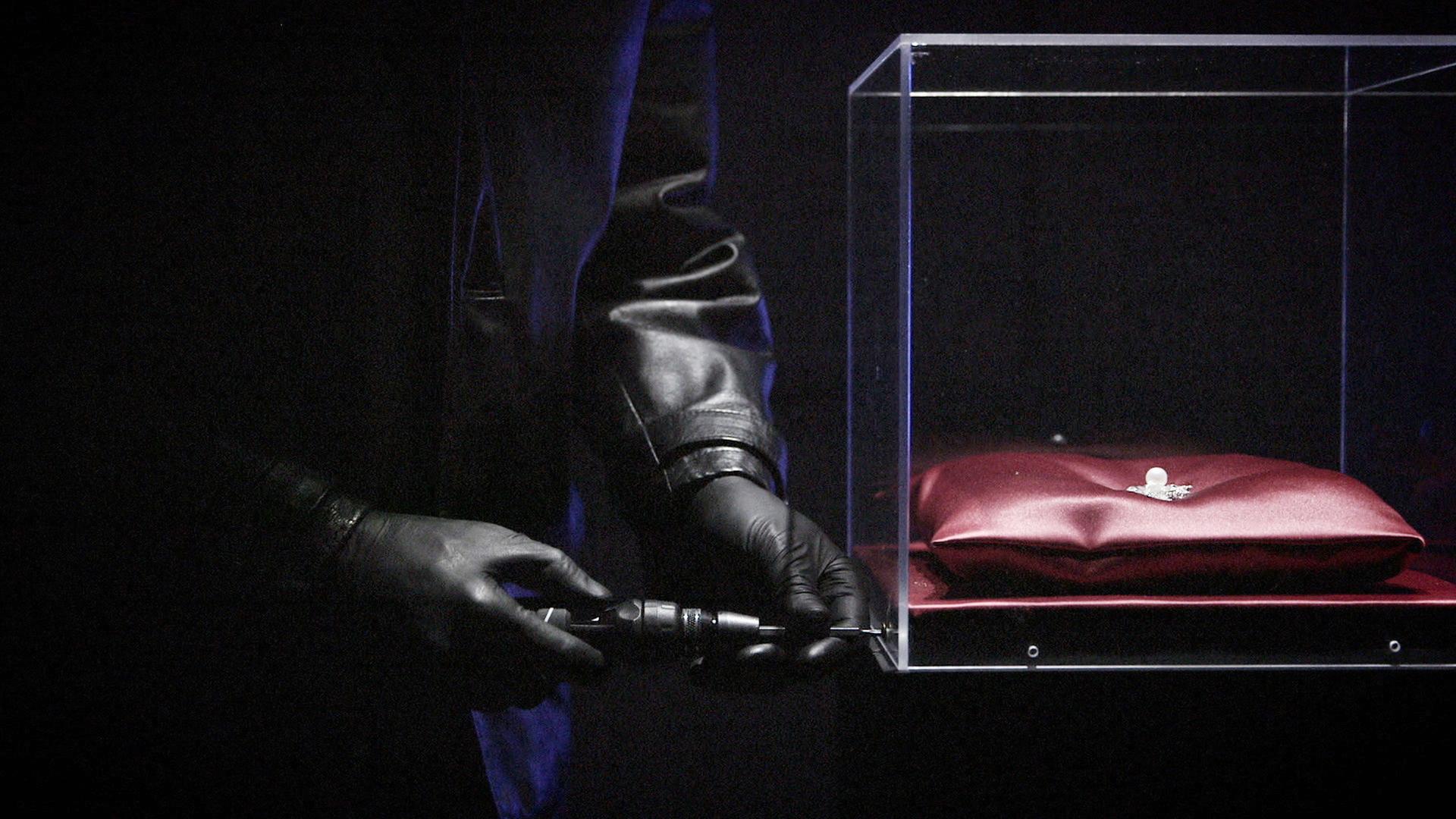 "Hightech-Gangster - Kaiserin Sisis geraubte Juwelen": Nachgestellte Szene: Zwei Hände in schwarzen Handschuhen halten einen Schraubenzieher, mit dem eine Glasvitrine geöffnet werden soll. Darin liegt auf einem roten Kissen der Sisi-Stern.