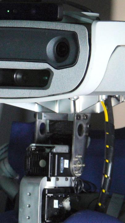 Nahaufnahme eines Roboters, dessen Aussehen menschliche Züge aufweist. Im Hintergrund ist ein Monitor zu erkennen.