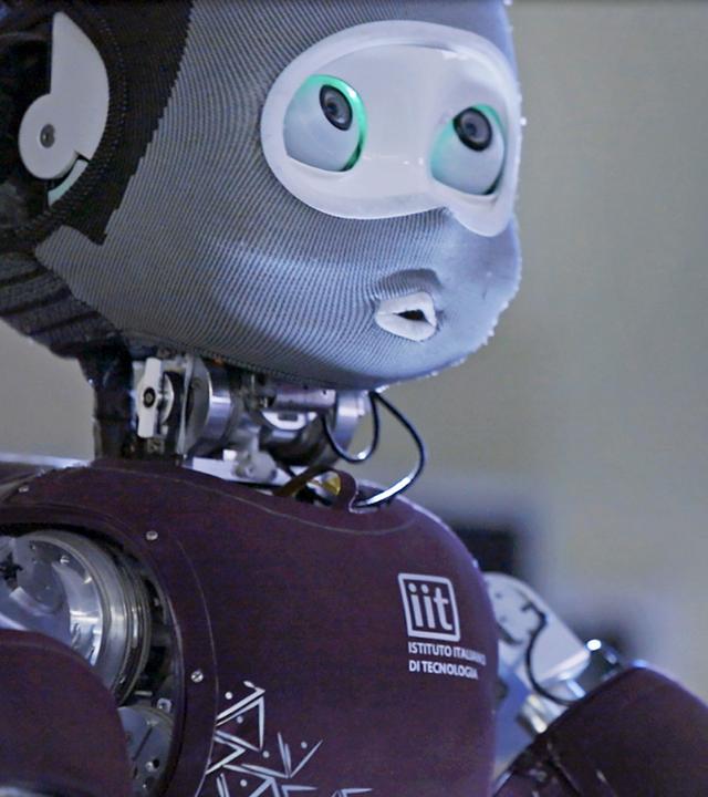 "Hightech Revolution - Sternstunden der Technik: Roboter": Nahaufnahme eines Roboters, dessen Aussehen menschliche Züge aufweist. Im Hintergrund ist ein Monitor zu erkennen.